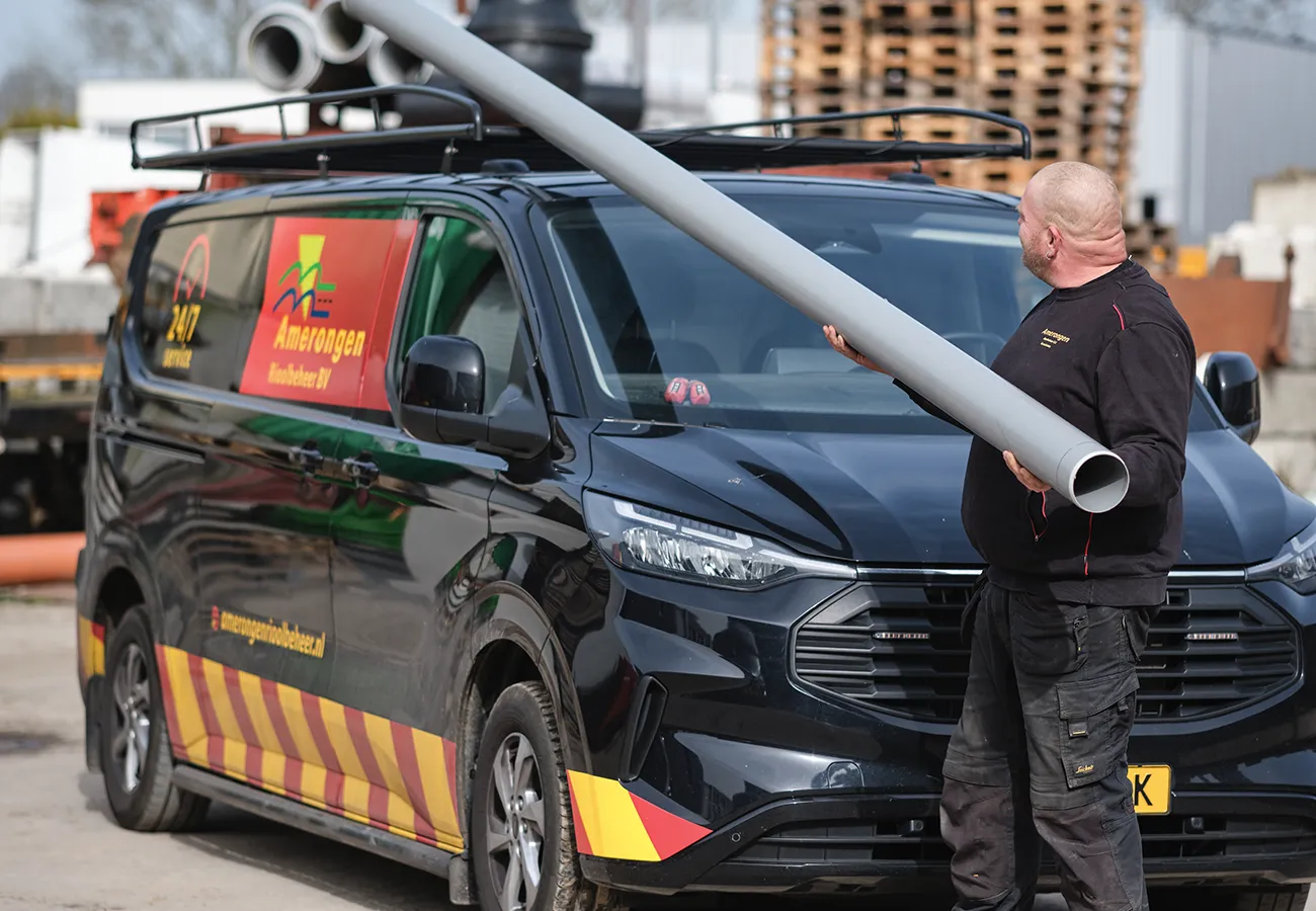 Medewerker van Amerongen Rioolbeheer met een regenpijp naast de bedrijfsbus