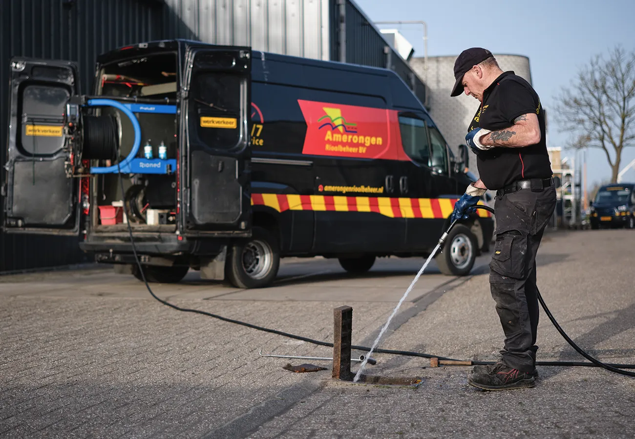 Medewerker van Amerongen Rioolbeheer met hogedrukapparatuur voor rioolreiniging bij de bedrijfsbus