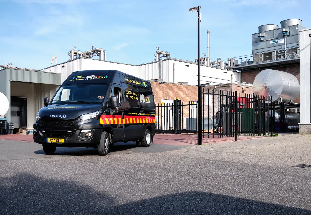 Bedrijfsbus van Amerongen Rioolbeheer rijdt weg bij een bedrijfslocatie, ingezet voor dakgootreiniging.