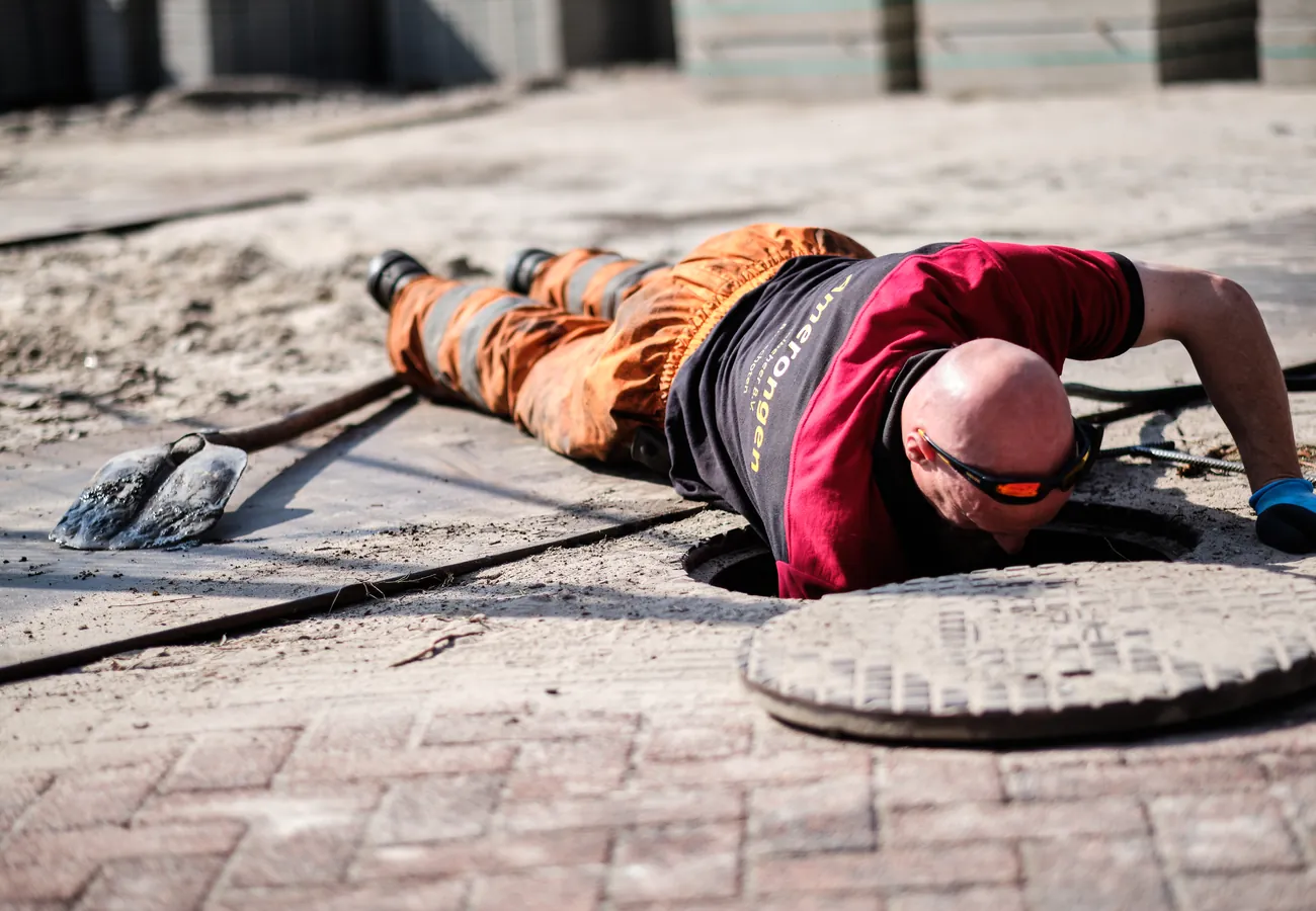 Monteur van Amerongen Rioolbeheer buigt zich over de rioolput met de reinigingsslang voor het ontstoppen van het riool in De Bilt